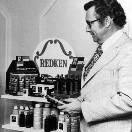 Homem, em preto e branco, segurando um produto de Redken.